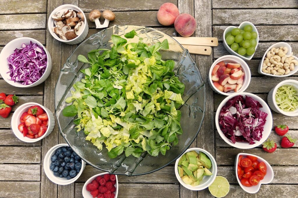 Various fruits and vegetables in bowls around a salad plate, representing foods cats should not eat.